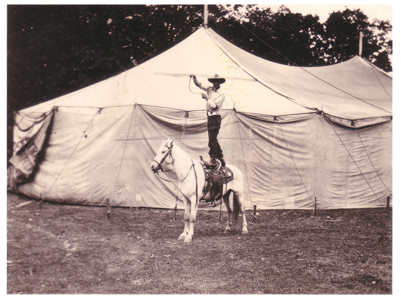 Bee Ho spinning a rope while standing on a horse in front of the tent for his own show, circa 1925.